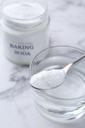 Photo of Glass of water and baking soda on white marble table, selective focus