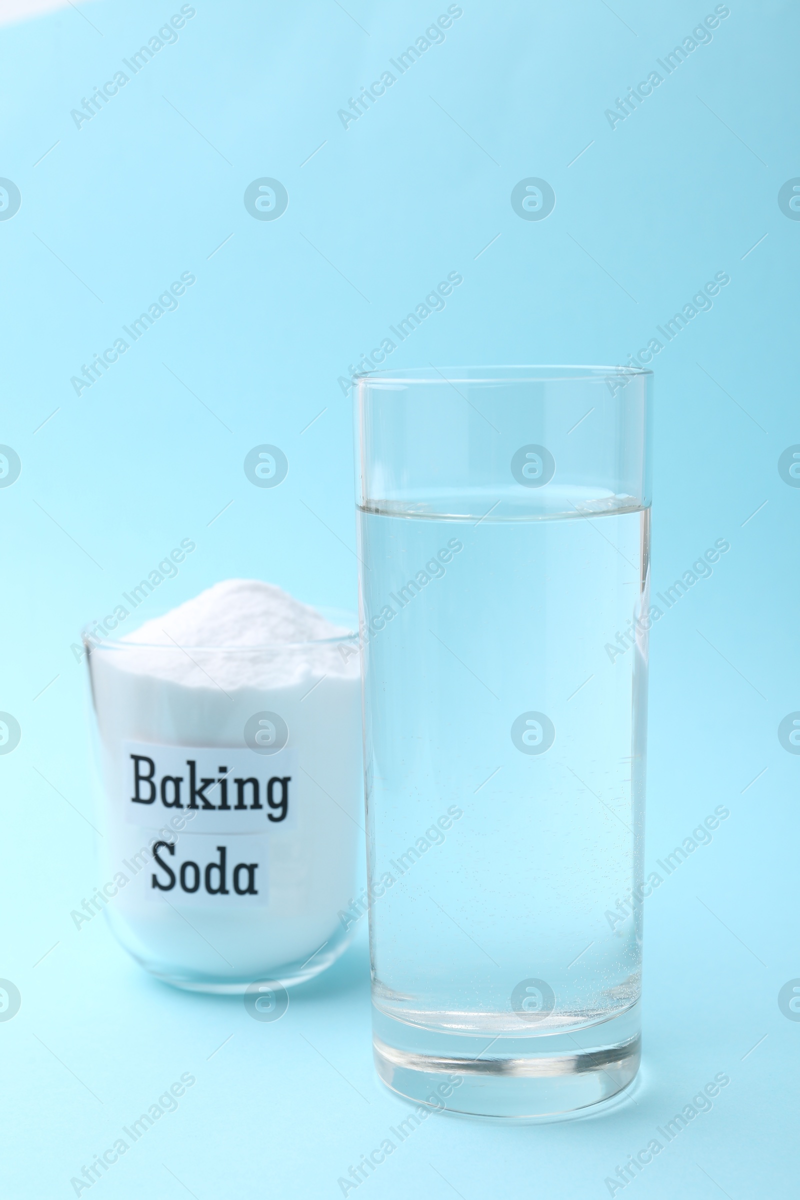 Photo of Glass of water and baking soda on light blue background