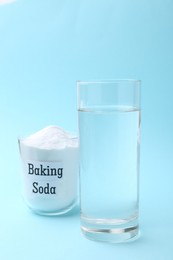 Glass of water and baking soda on light blue background