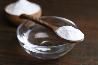 Glass of water and baking soda on wooden table, closeup