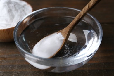 Adding baking soda into bowl of water at wooden table, closeup