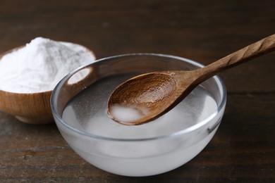 Adding baking soda into bowl of water at wooden table, closeup