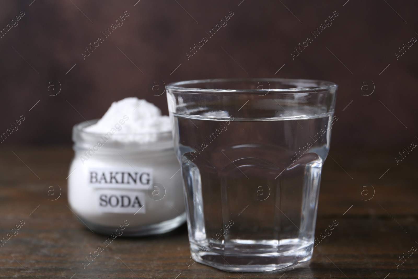 Photo of Glass of water and baking soda on wooden table, selective focus