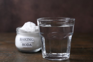 Glass of water and baking soda on wooden table, selective focus