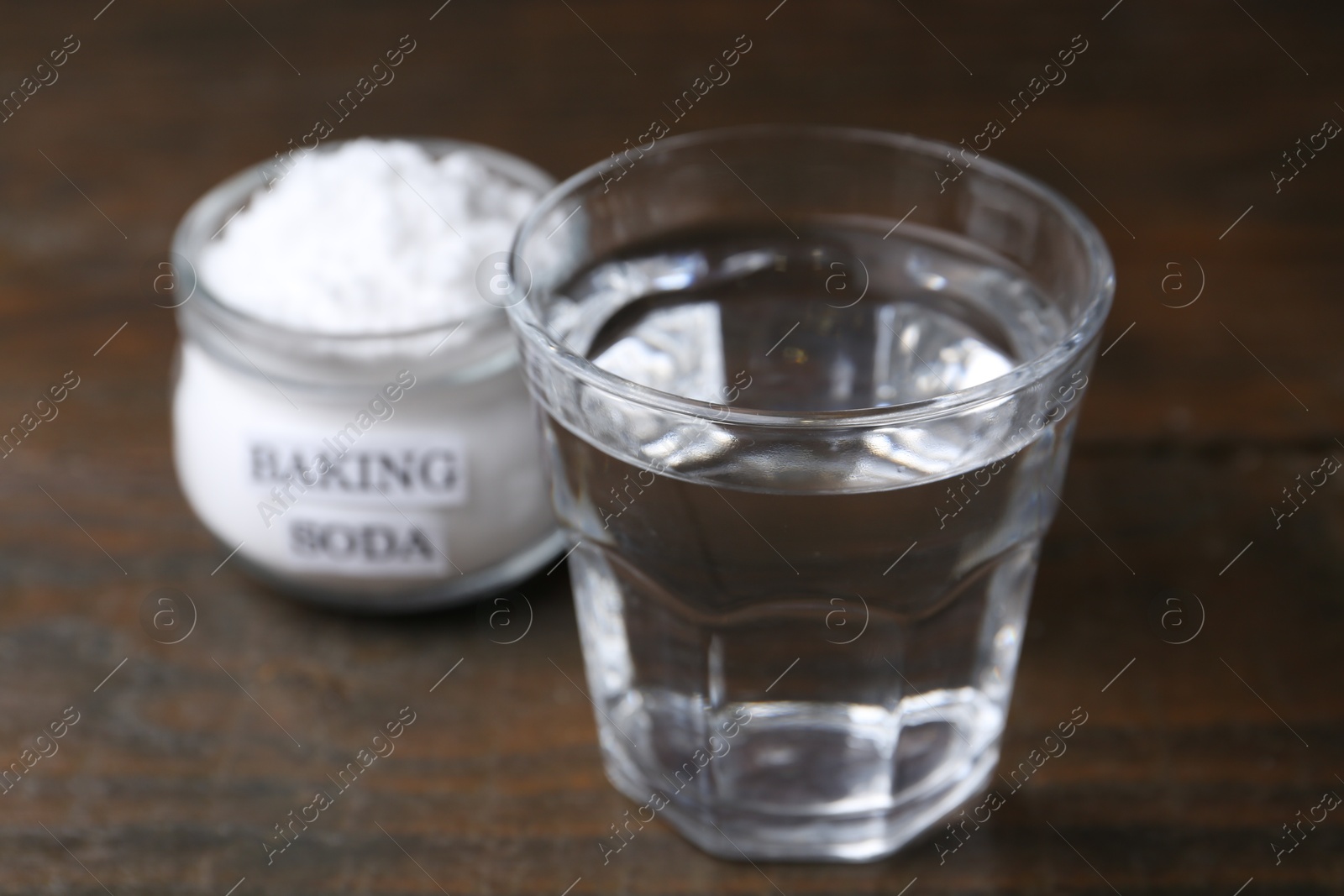 Photo of Glass of water and baking soda on wooden table, selective focus