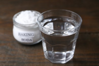 Glass of water and baking soda on wooden table, selective focus