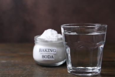 Glass of water and baking soda on wooden table, selective focus. Space for text