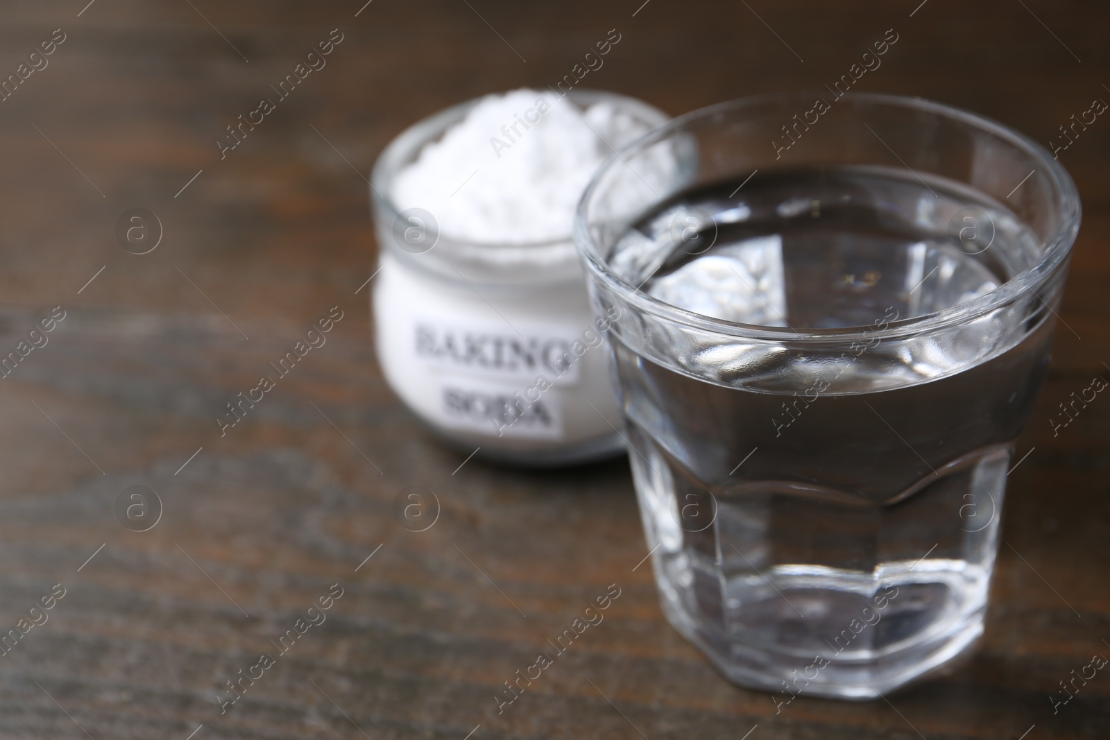 Photo of Glass of water and baking soda on wooden table, selective focus. Space for text