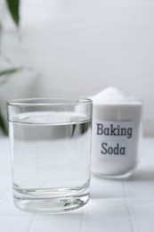 Glass of water and baking soda on white tiled table. Space for text