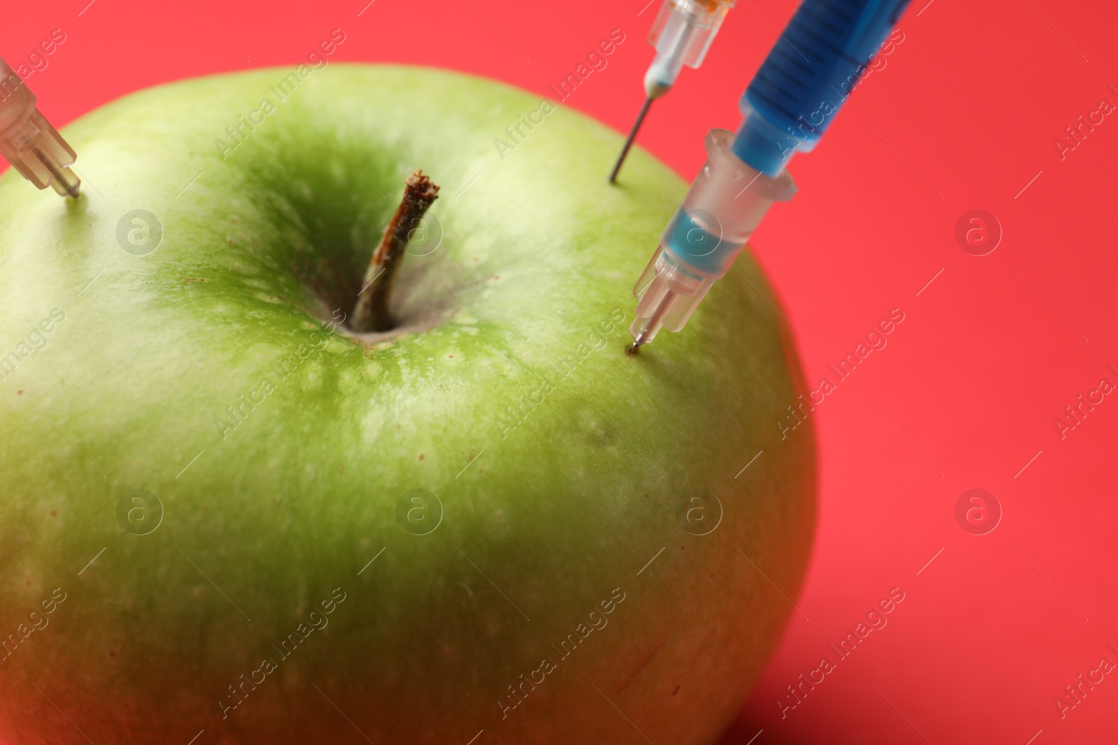 Photo of GMO concept. Green apple with different syringes on red background, closeup