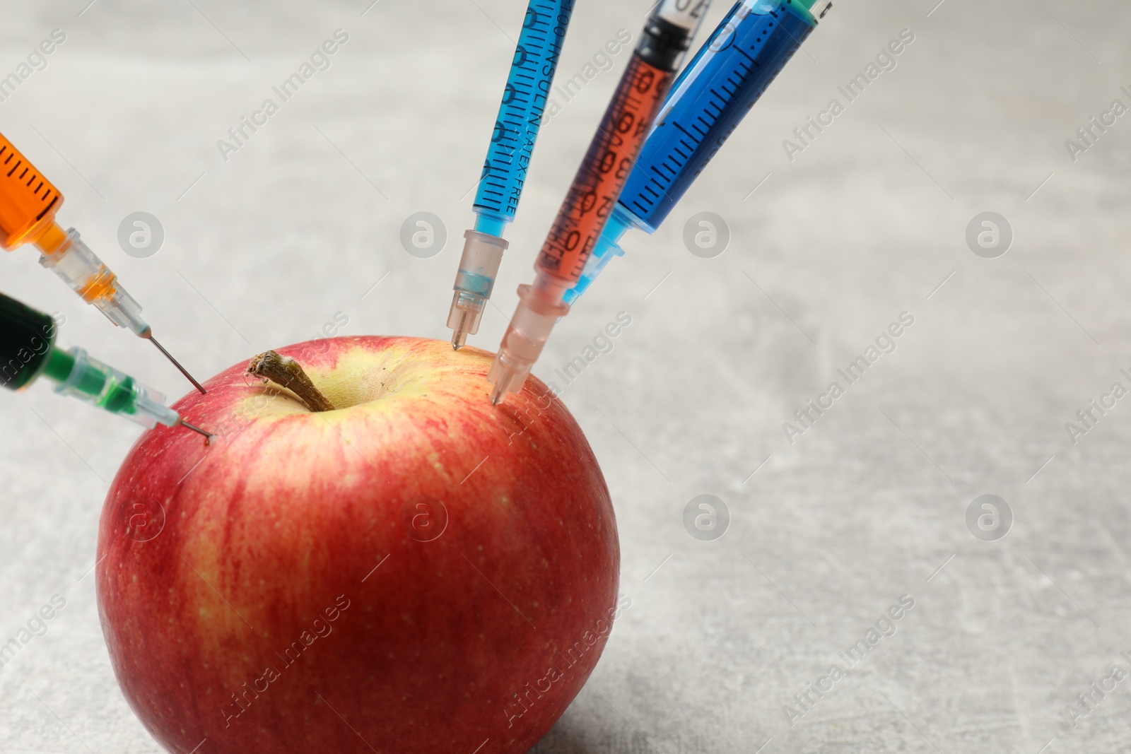 Photo of GMO concept. Red apple with syringes on grey textured table, closeup