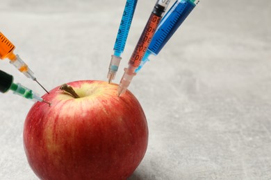 Photo of GMO concept. Red apple with syringes on grey textured table, closeup