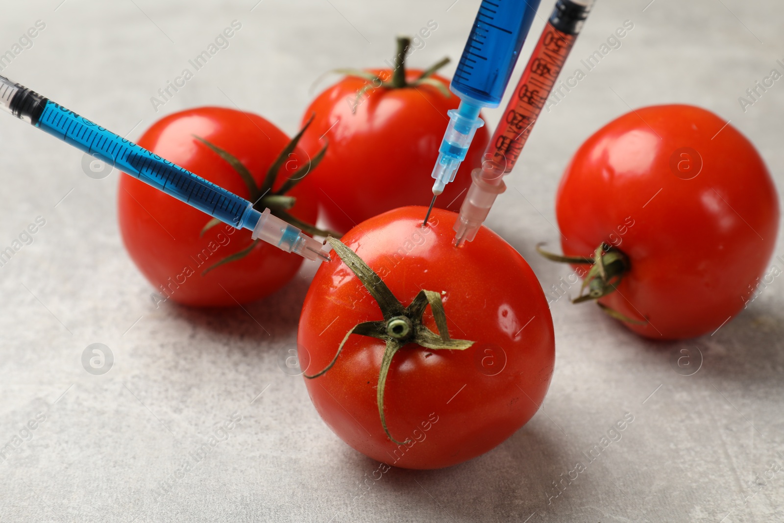 Photo of GMO concept. Tomato with different syringes on grey textured table, closeup