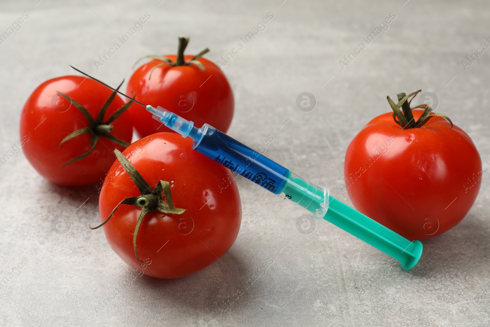 Photo of GMO concept. Tomatoes and syringe with liquid on grey textured table, closeup