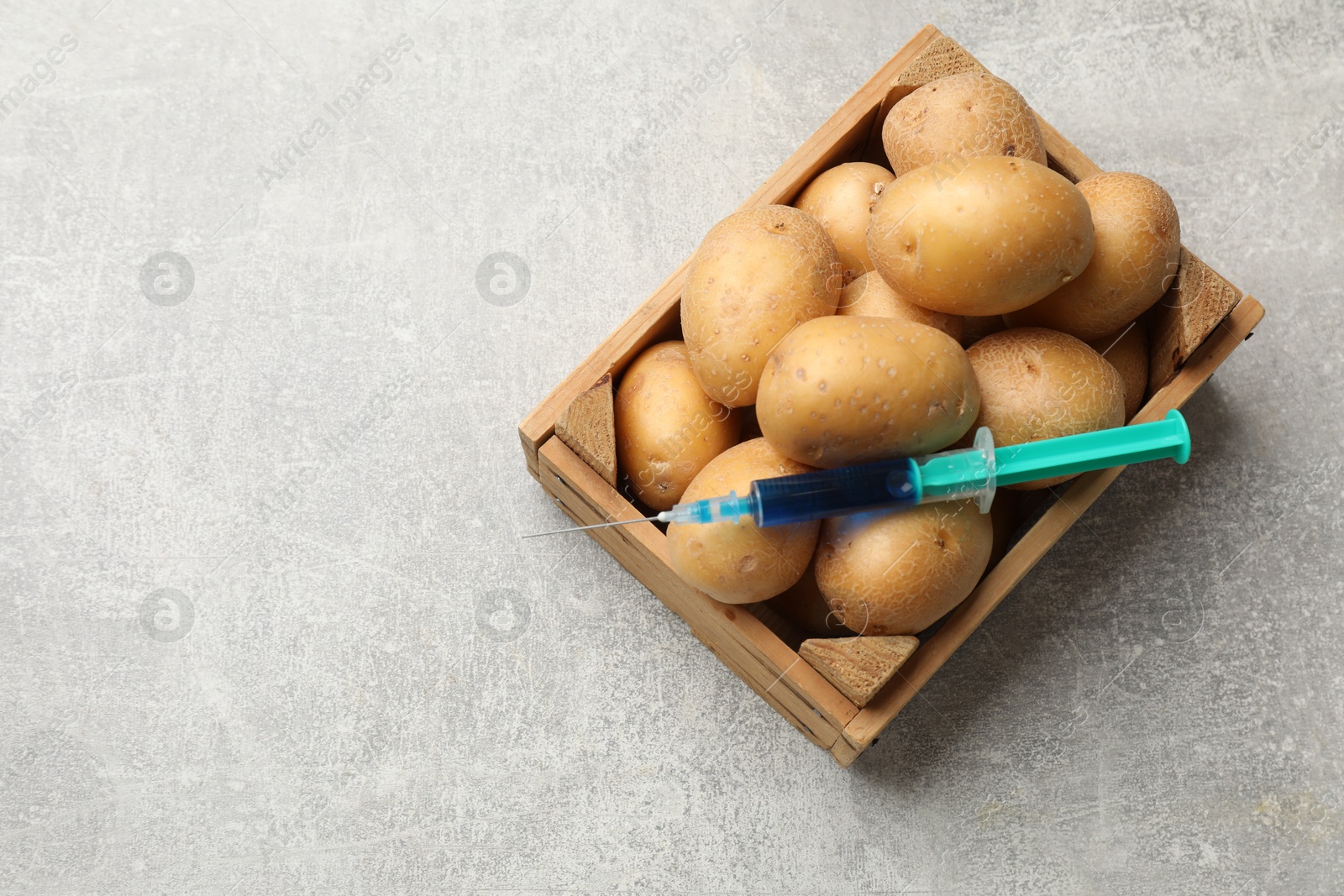 Photo of GMO concept. Potatoes and syringe with liquid in crate on grey textured table, top view. Space for text