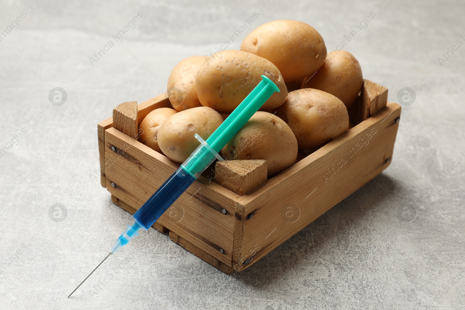 Photo of GMO concept. Potatoes and syringe with liquid in crate on grey textured table, closeup