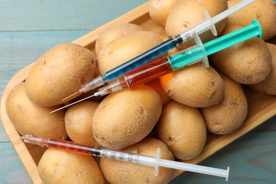 Photo of GMO concept. Potatoes and syringes with liquid on light blue wooden table, top view