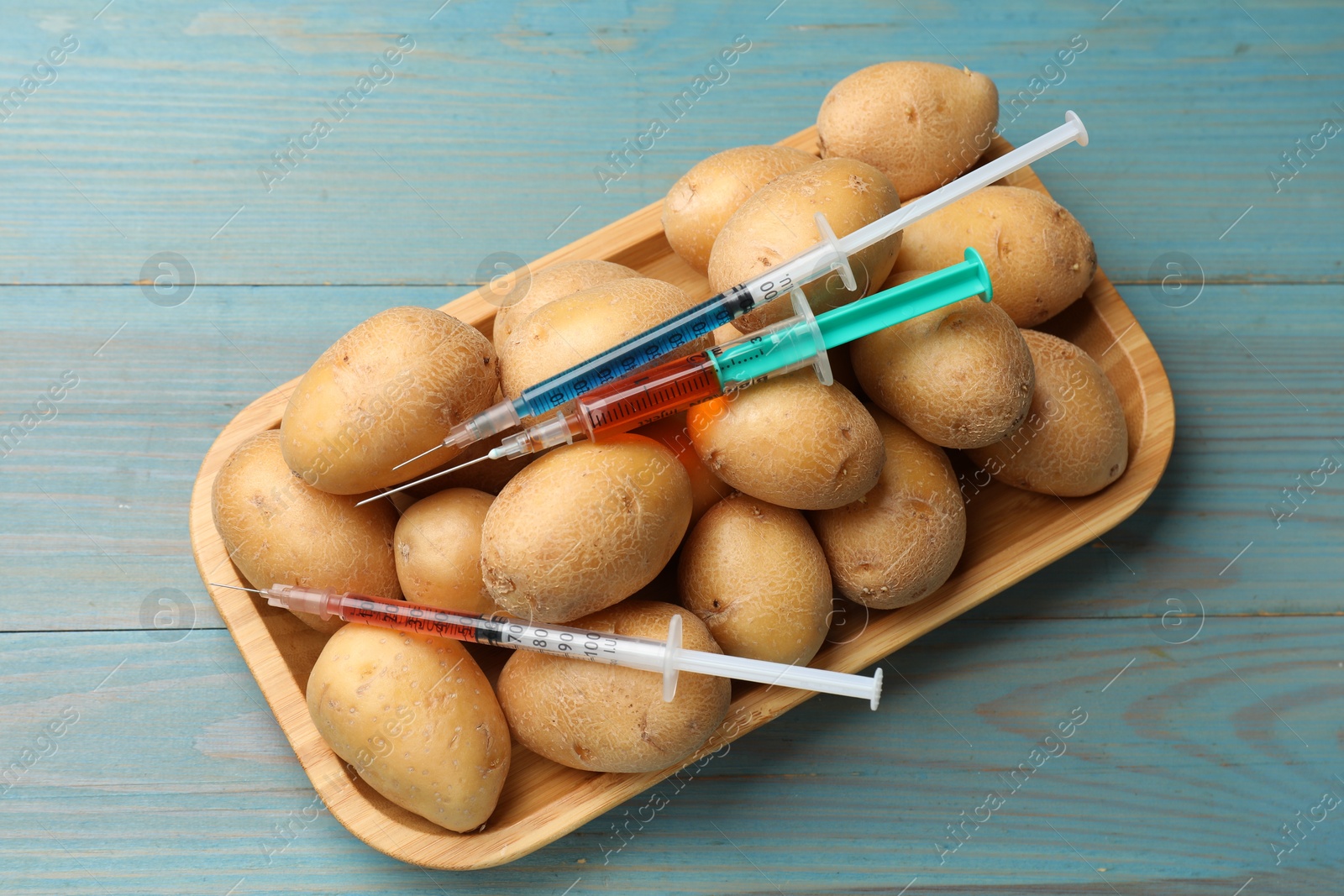 Photo of GMO concept. Potatoes and syringes with liquid on light blue wooden table, top view