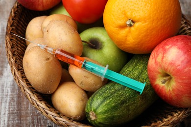 Photo of GMO concept. Different products and syringe in basket on wooden table, closeup