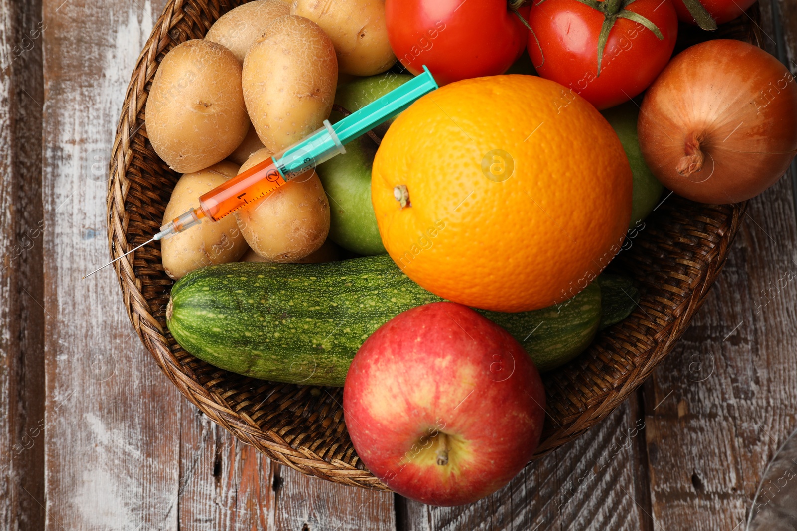 Photo of GMO concept. Different products and syringe in basket on wooden table, top view