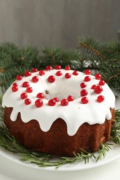 Photo of Beautifully decorated Christmas cake and fir branches on white table, closeup