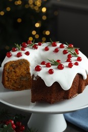 Photo of Traditional Christmas cake decorated with red currants and rosemary on table against blurred lights