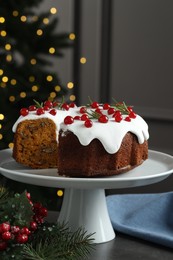 Photo of Traditional Christmas cake decorated with red currants and rosemary on gray table against blurred lights