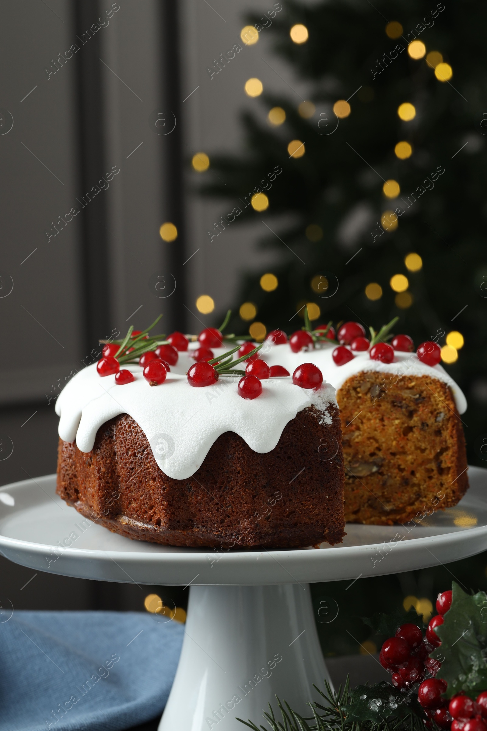 Photo of Traditional Christmas cake decorated with red currants and rosemary on table against blurred lights