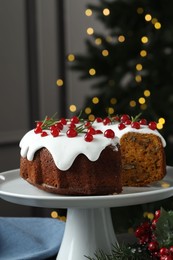 Photo of Traditional Christmas cake decorated with red currants and rosemary on table against blurred lights