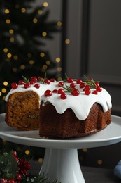 Photo of Traditional Christmas cake decorated with red currants and rosemary on table against blurred lights