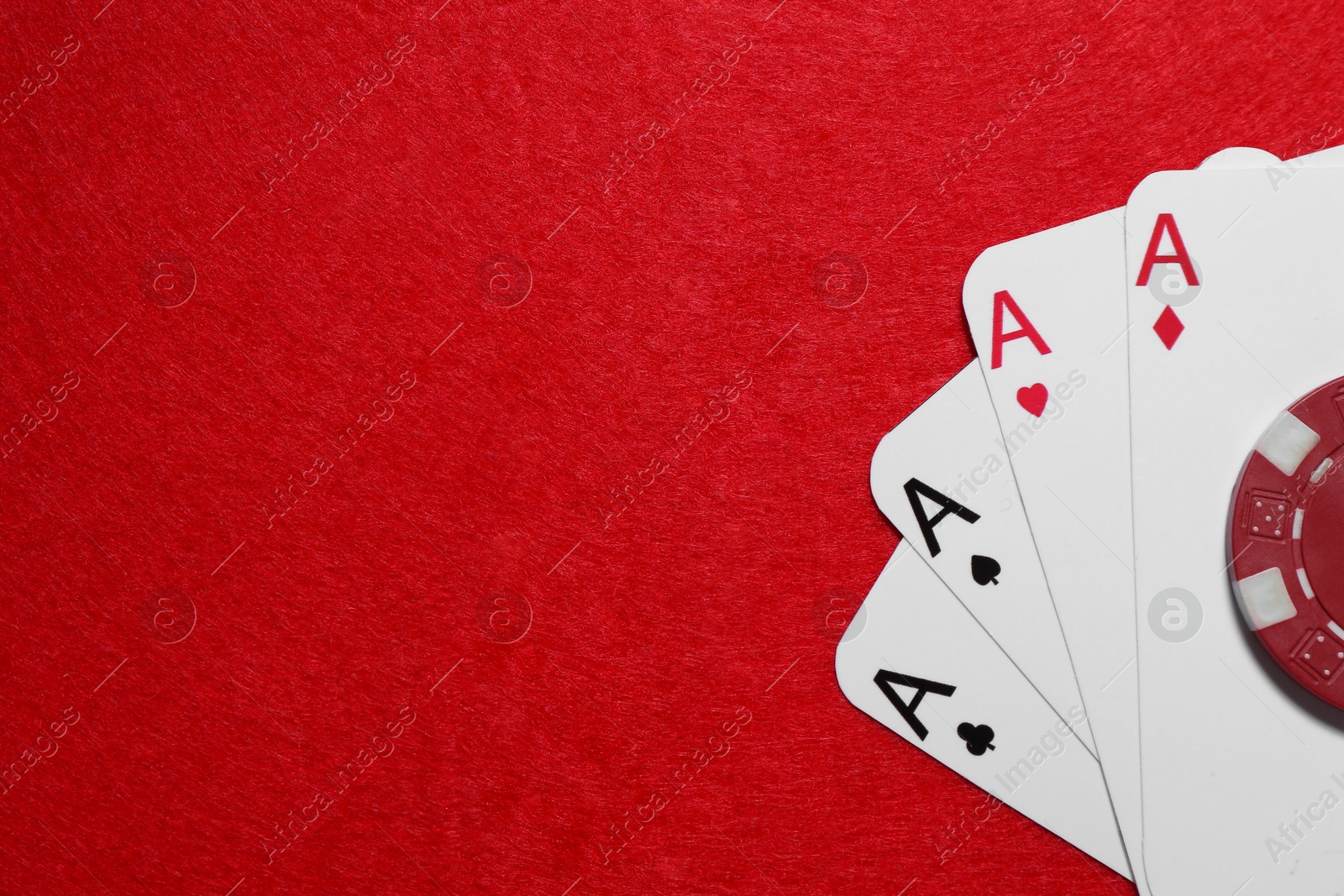 Photo of Playing cards and poker chip on red table, top view. Space for text