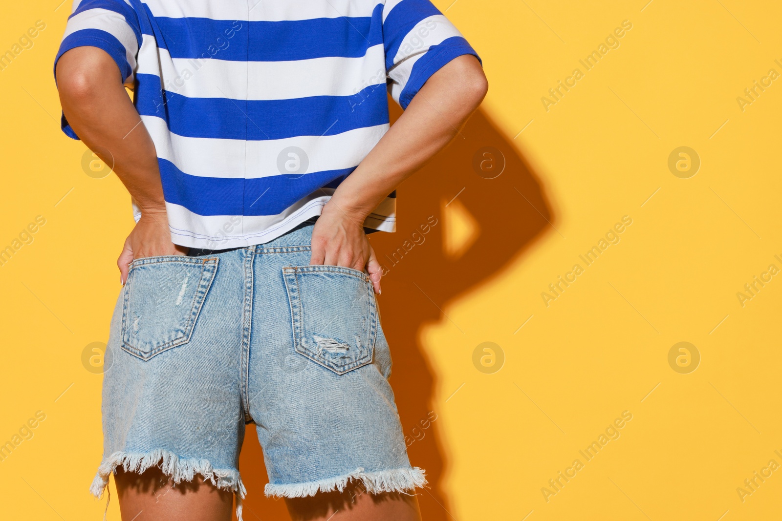 Photo of Woman wearing stylish denim shorts on yellow background, closeup. Space for text