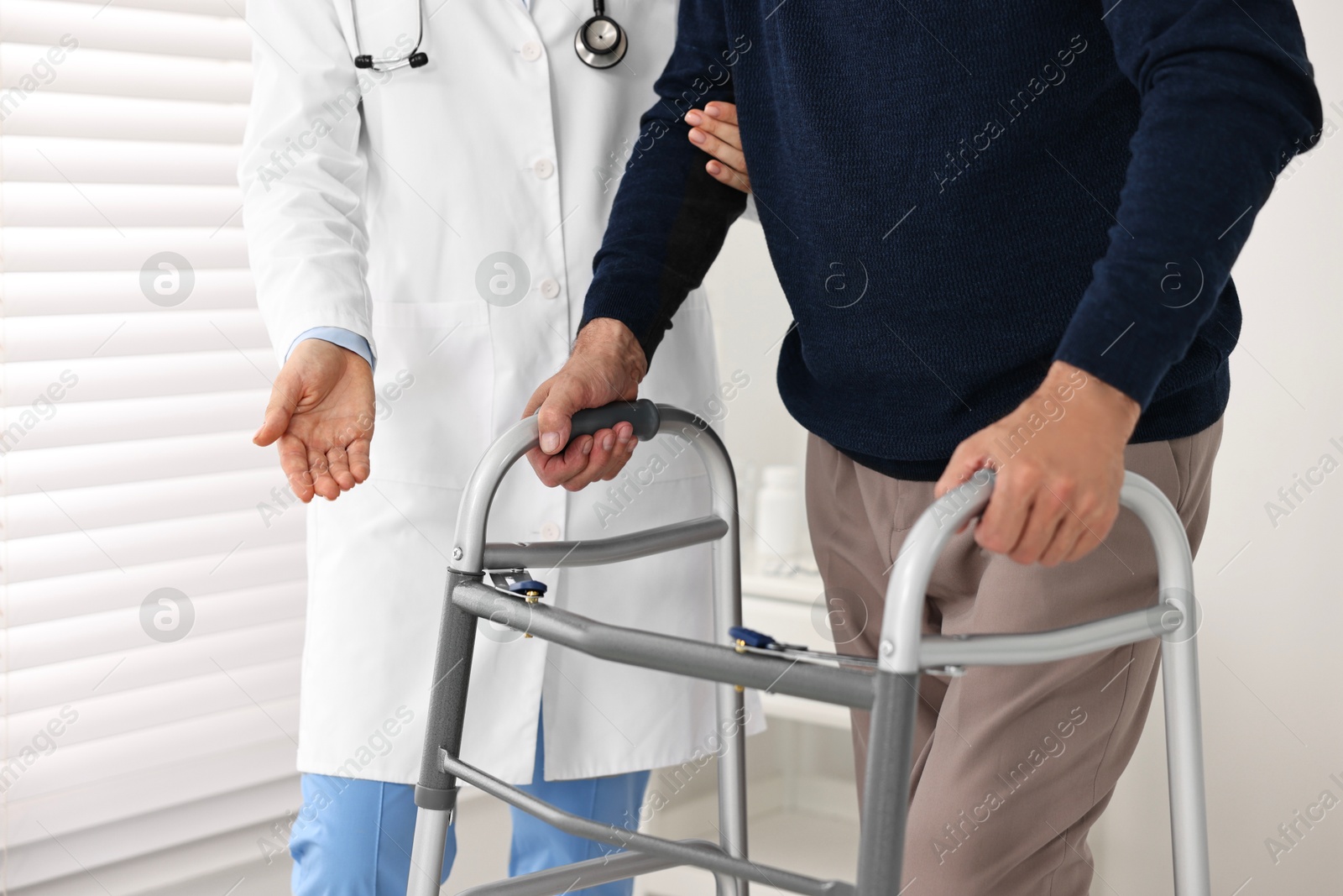 Photo of Doctor helping senior man with walking frame in clinic, closeup