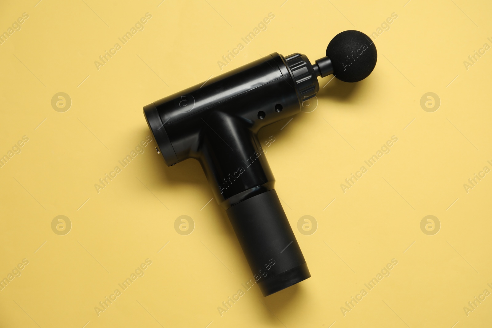 Photo of One black percussive massager on yellow background, top view