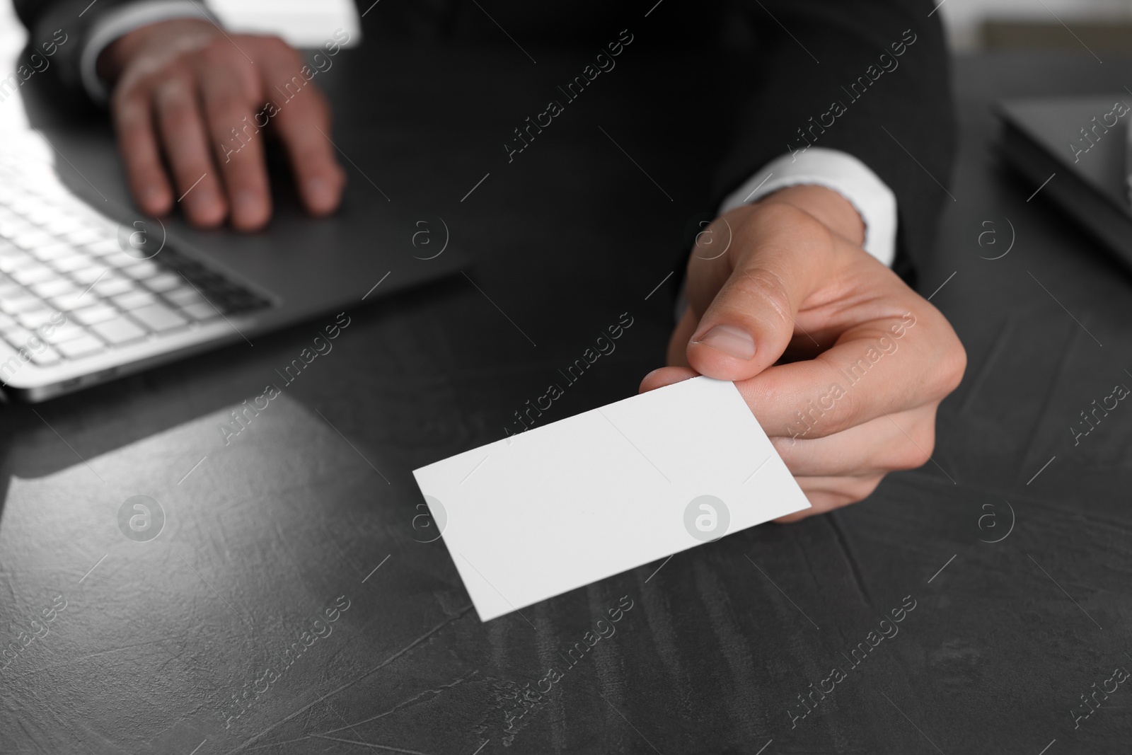 Photo of Man holding blank business card at table in office, closeup. Mockup for design