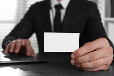 Photo of Man holding blank business card at table in office, closeup. Mockup for design