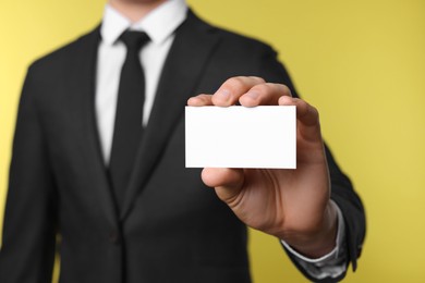 Photo of Man holding blank business card on yellow background, closeup. Mockup for design