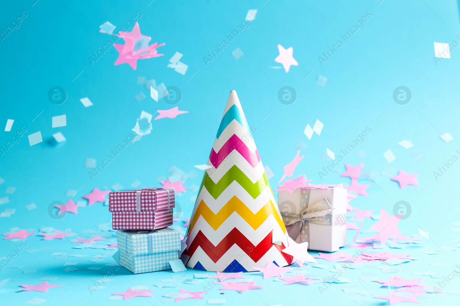 Photo of Beautiful confetti falling on party hat and gift boxes against light blue background