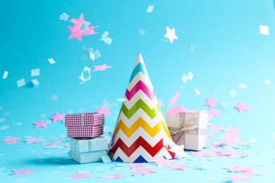 Photo of Beautiful confetti falling on party hat and gift boxes against light blue background