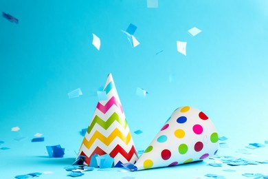 Photo of Beautiful confetti falling on party hats against light blue background