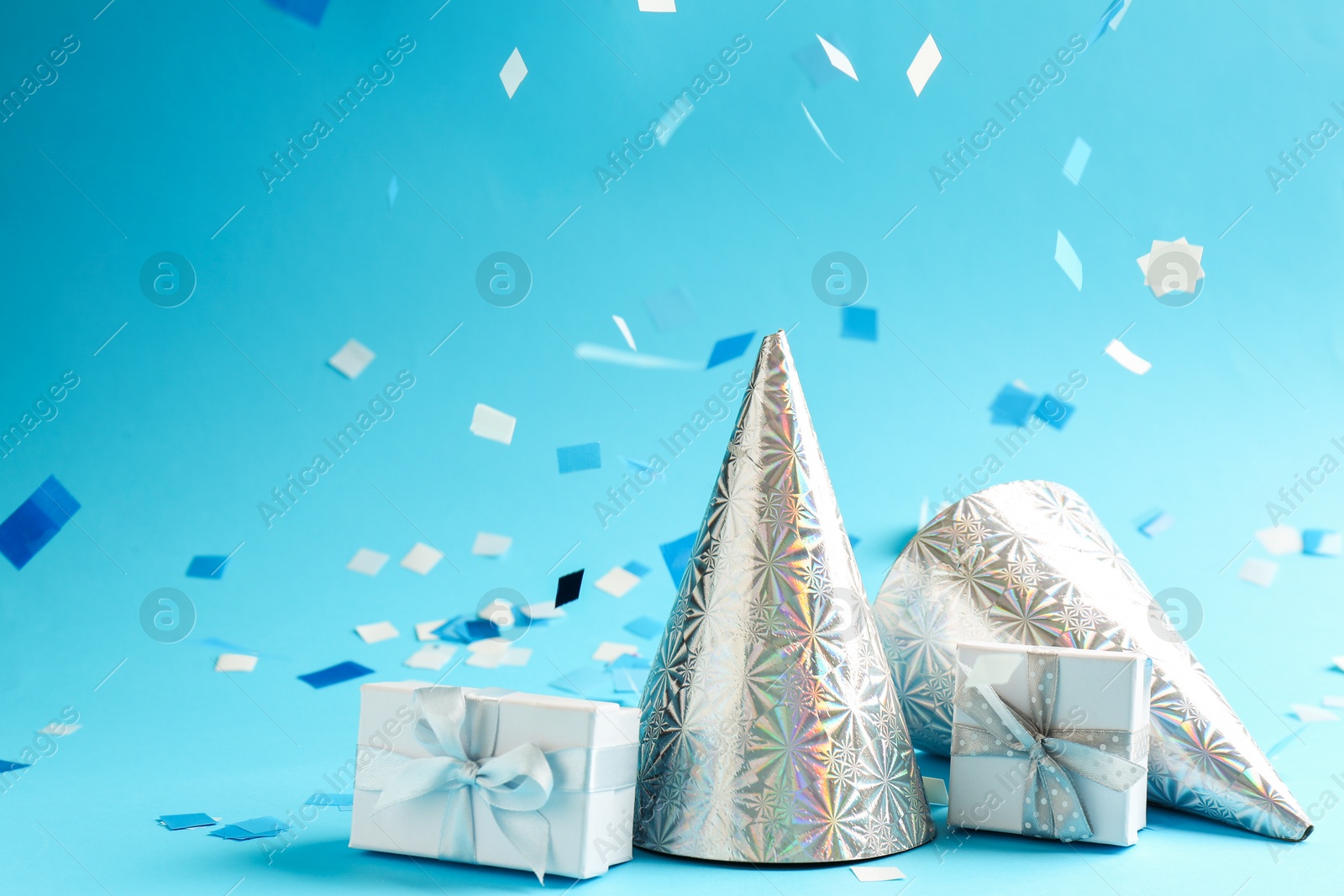 Photo of Beautiful confetti, gift boxes and party hats on light blue background, closeup. Space for text