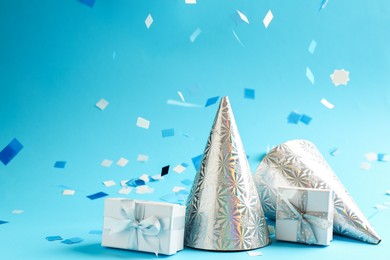 Photo of Beautiful confetti, gift boxes and party hats on light blue background, closeup. Space for text