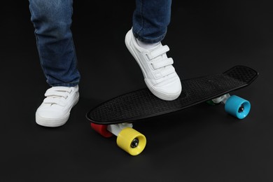 Photo of Little boy with skateboard on black background, closeup