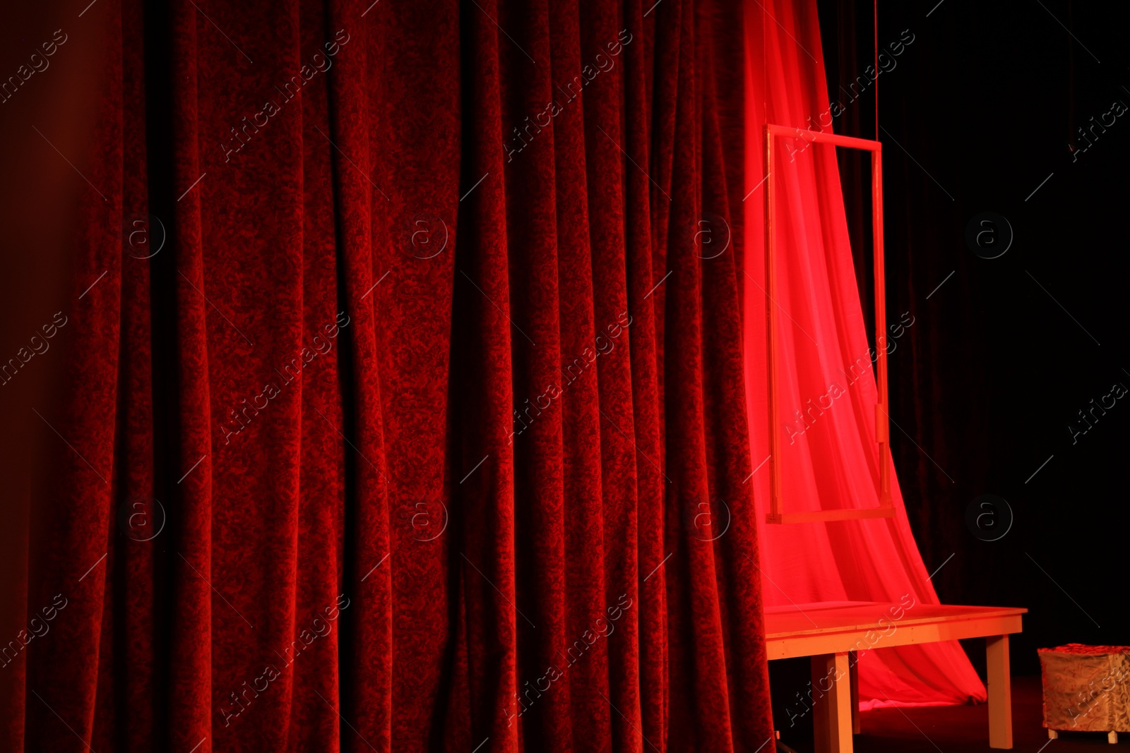 Photo of Elegant red curtains, table and frame on stage in theatre