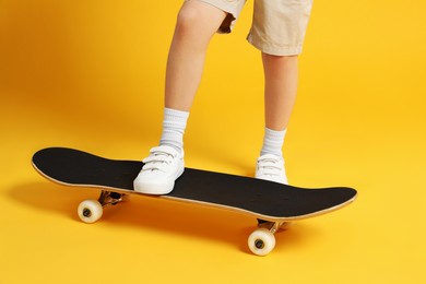 Little girl with skateboard on yellow background, closeup