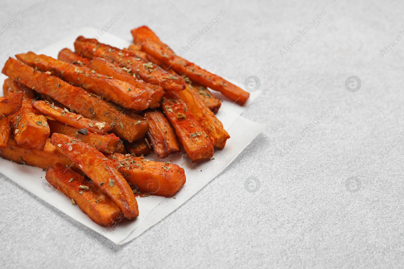 Photo of Delicious sweet potato fries with spices on light grey table, closeup. Space for text