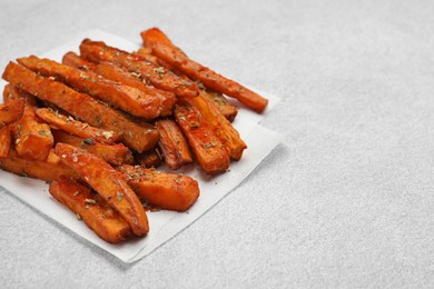 Photo of Delicious sweet potato fries with spices on light grey table, closeup. Space for text