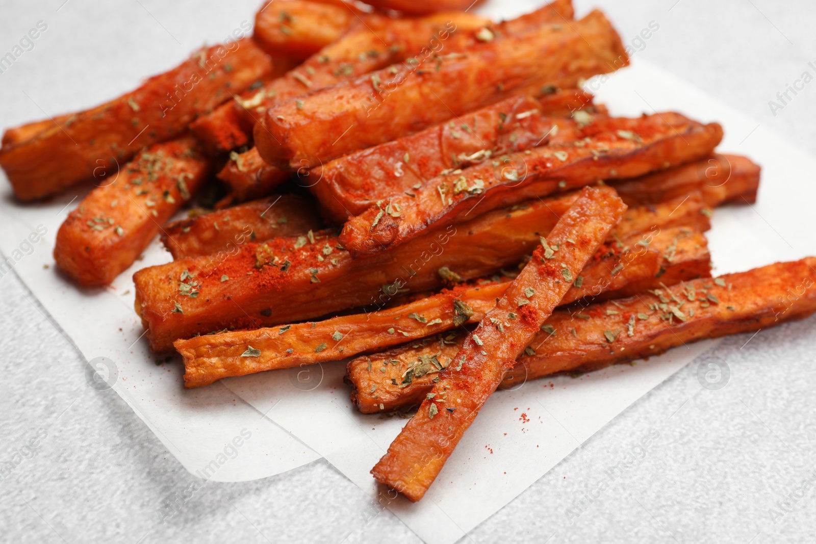 Photo of Delicious sweet potato fries with spices on light grey table, closeup