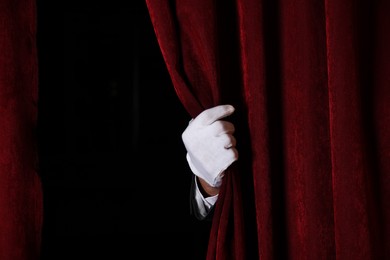 Photo of Man opening red front curtains in theatre, closeup