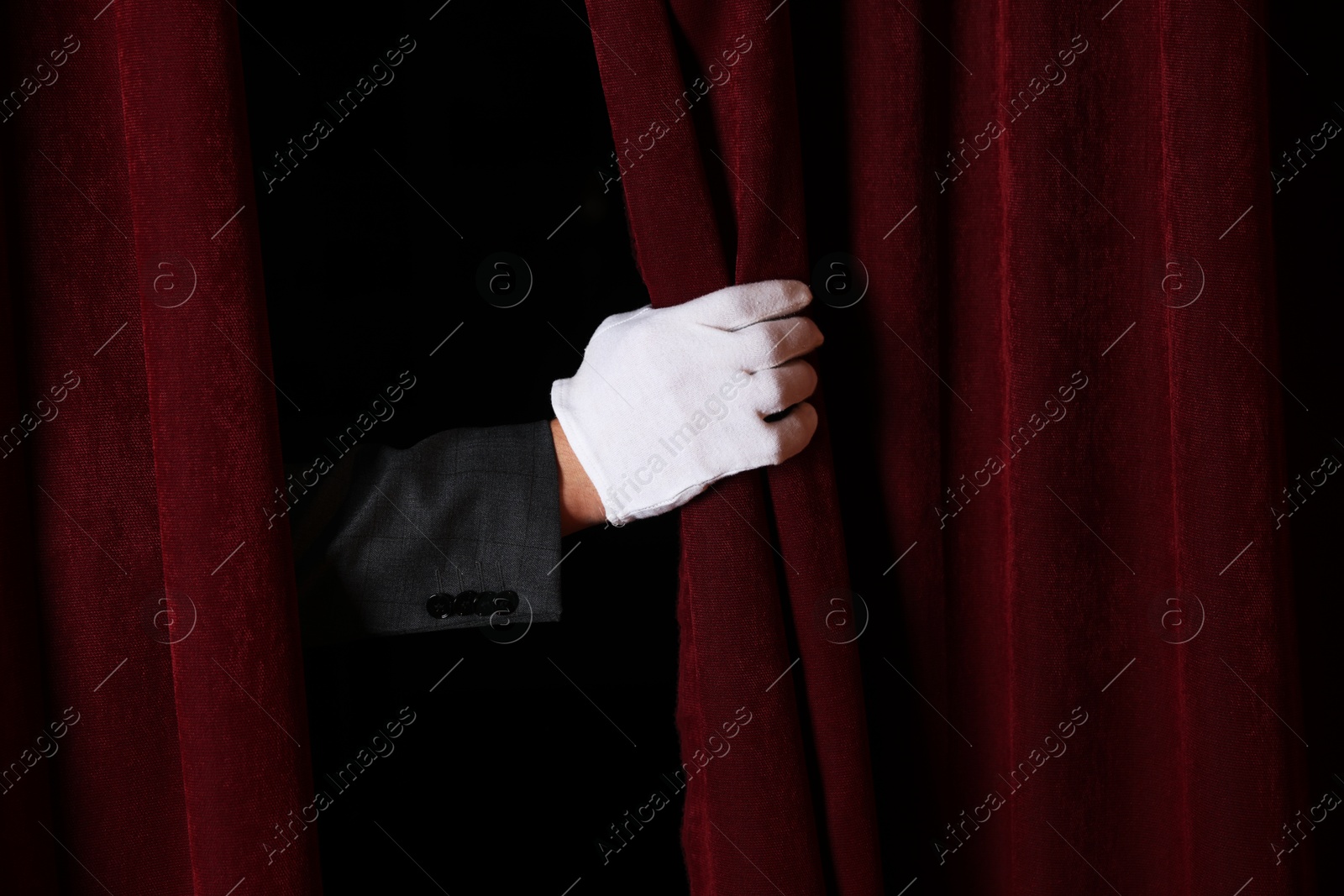 Photo of Man closing red front curtains in theatre, closeup